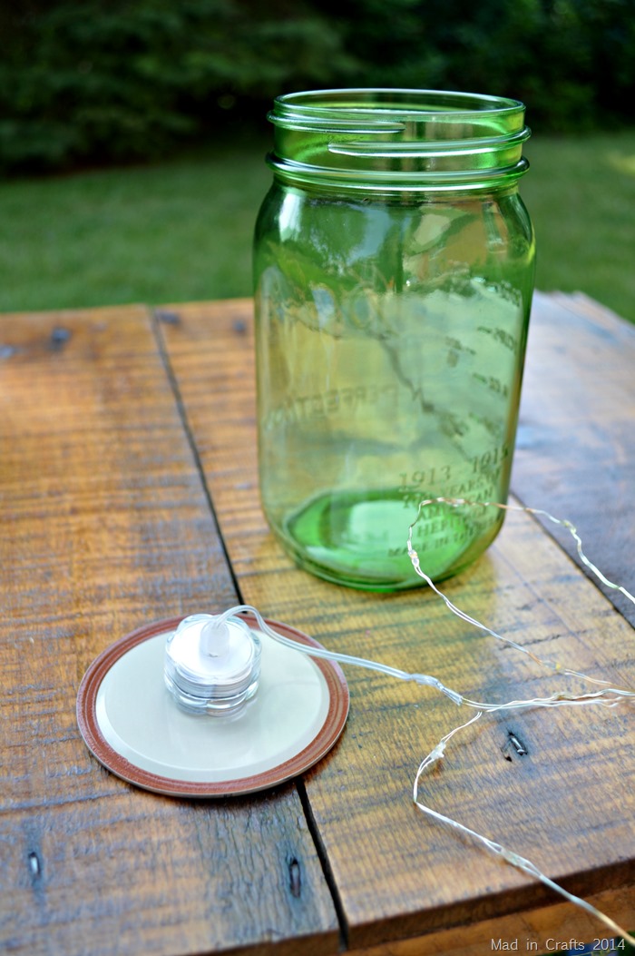 Green mason jar on a table. A string of mini LED lights is glued to the inside of the jar's lid insert