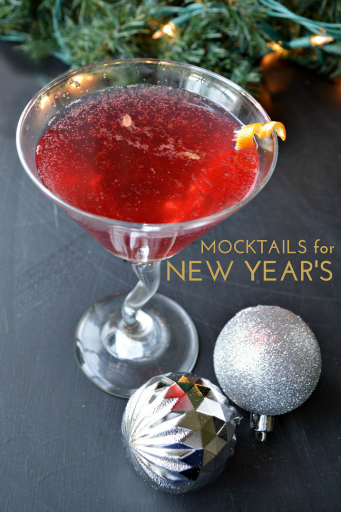 close up of a red drink in a martini glass and christmas ornaments on a black background