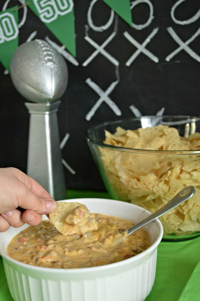 hand holding chip with queso and bowl of chips