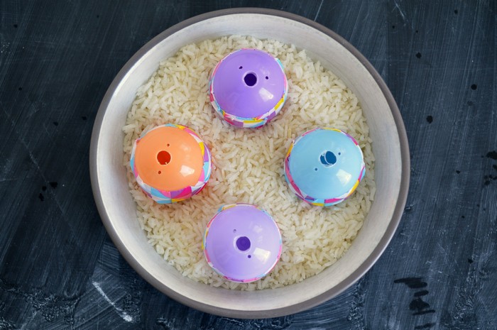 four plastic eggs with holes drilled in the bottom sitting in a bowl of uncooked rice