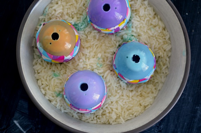four plastic eggs filled with liquid soap sitting in a bowl of uncooked rice
