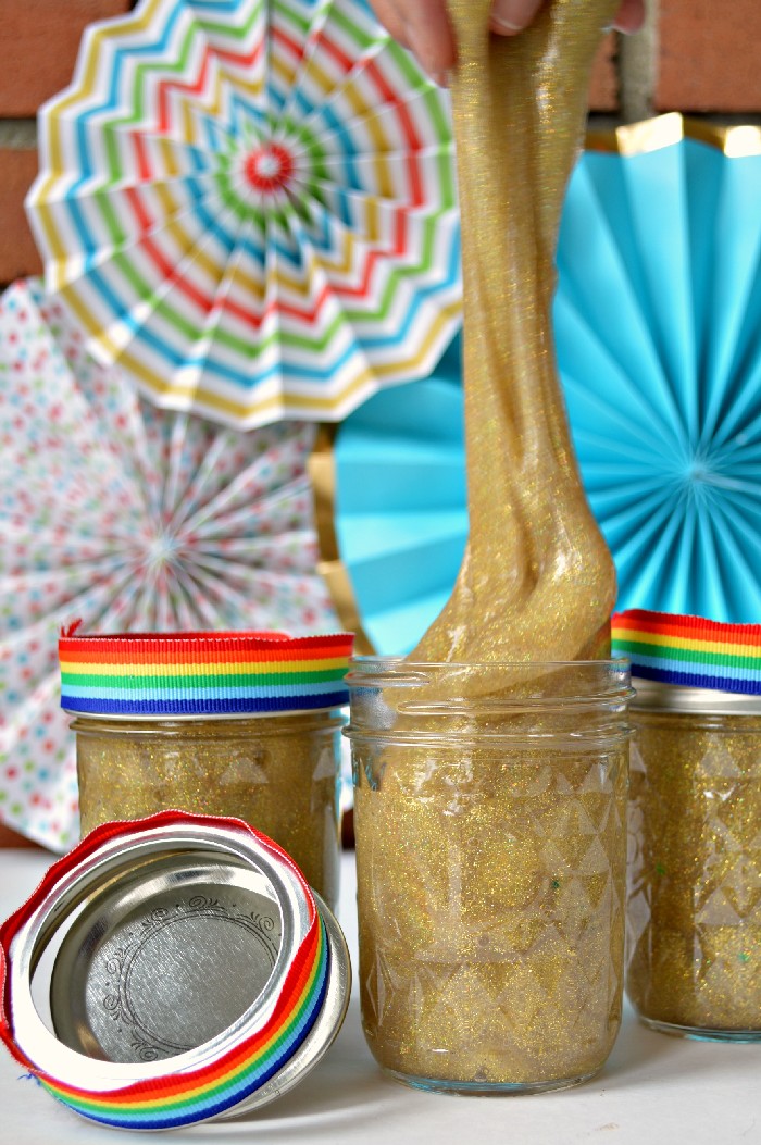 Hand pulling gold slime from a mason jar with a colorful background