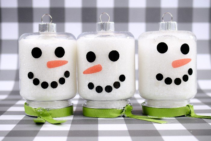 three jar ornaments decorated with snowman faces on a black and white plaid background