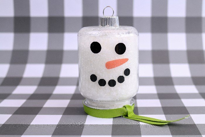 a jar ornaments filled with Epsom salts and decorated with snowman faces on a black and white plaid background