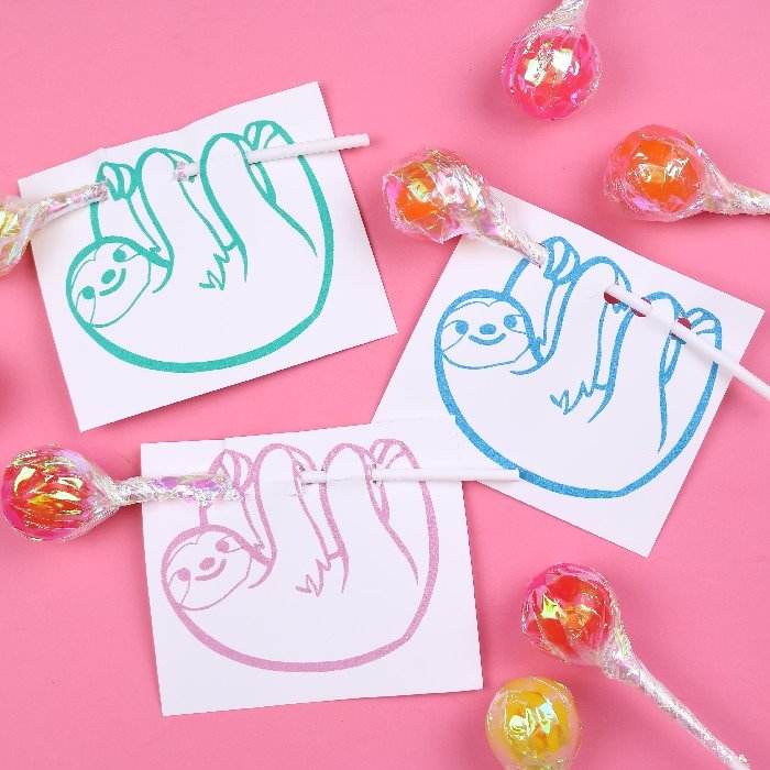 3 colorful sloth valentine cards that hold lollipops on a pink background