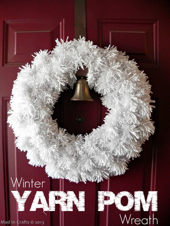 White yarn pom pom wreath on a red door