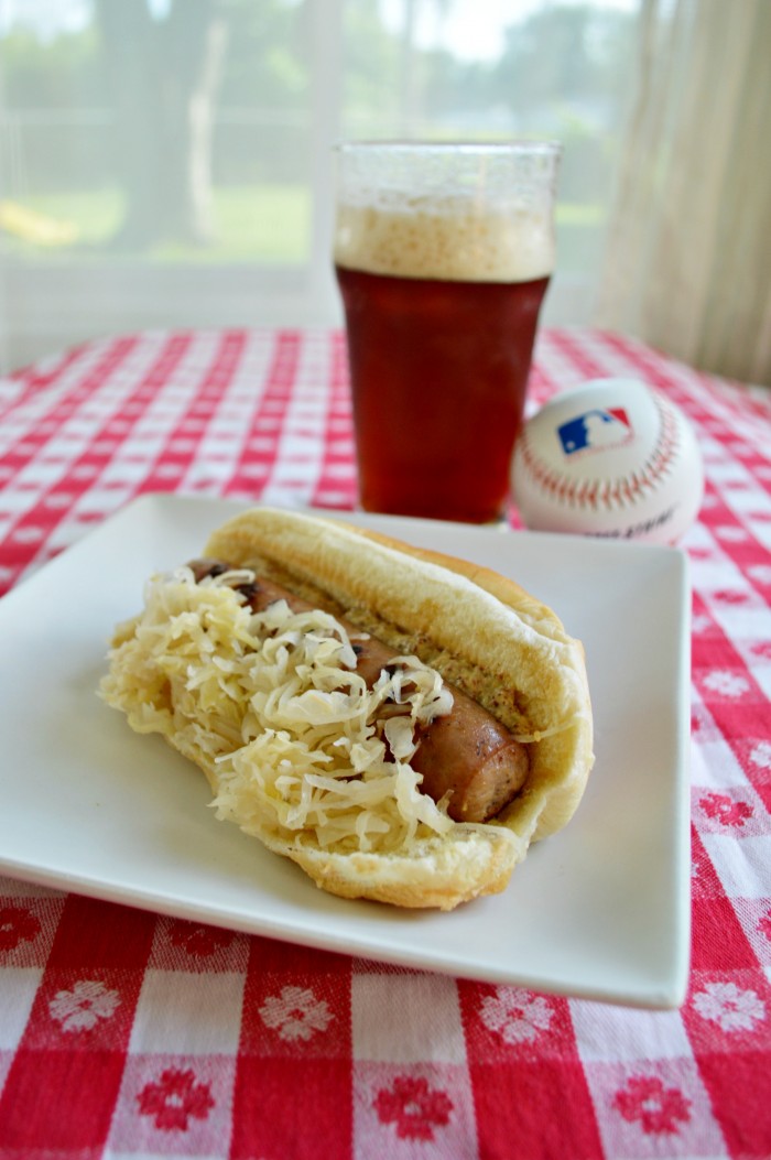 a sauerkraut topped brat on a white plate near a glass of beer