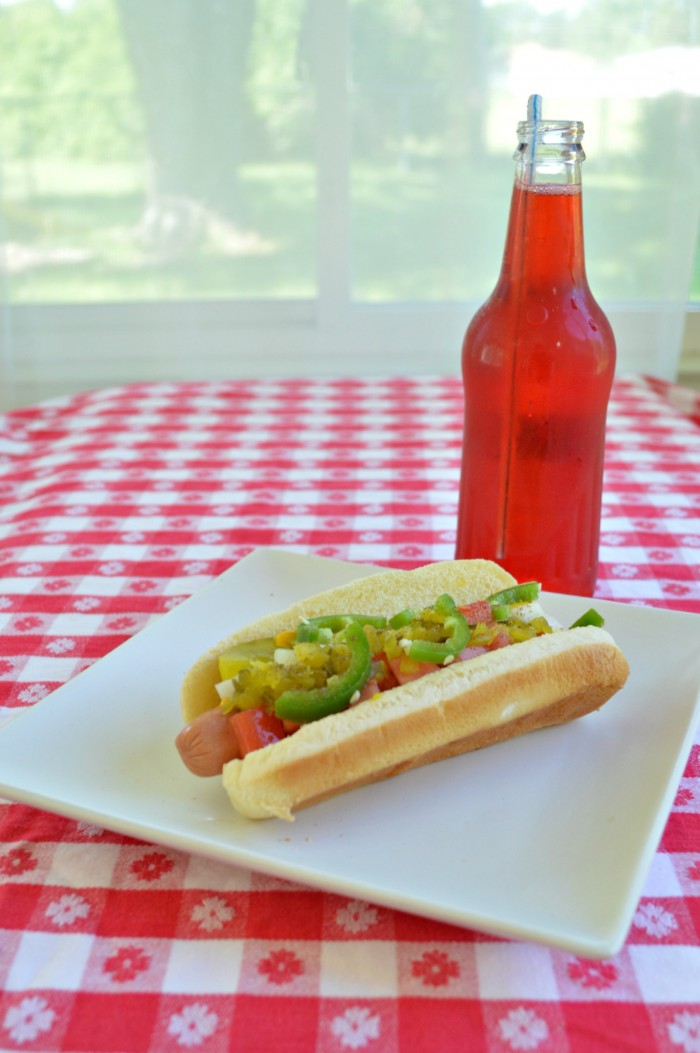 a glass bottle of red pop near a Chicago style hot dog