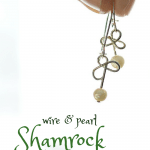 hand holding wire and pearl shamrock earrings on a white background