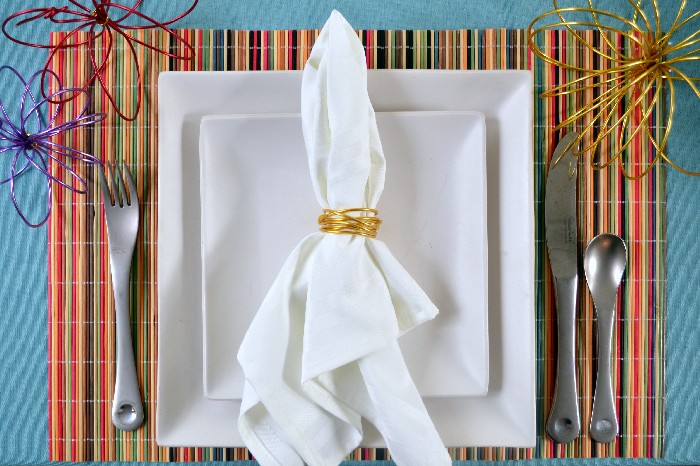 wrapped wire napkin ring holding white napkin on square white plates and a colorful placemat