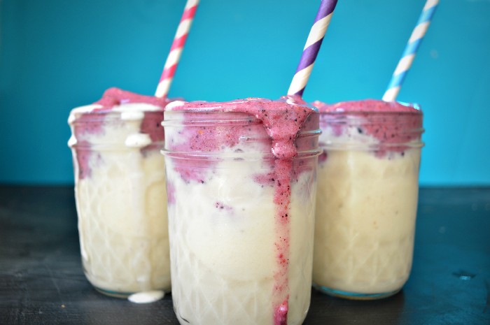 three mason jars filled with layered berry smoothies and straws