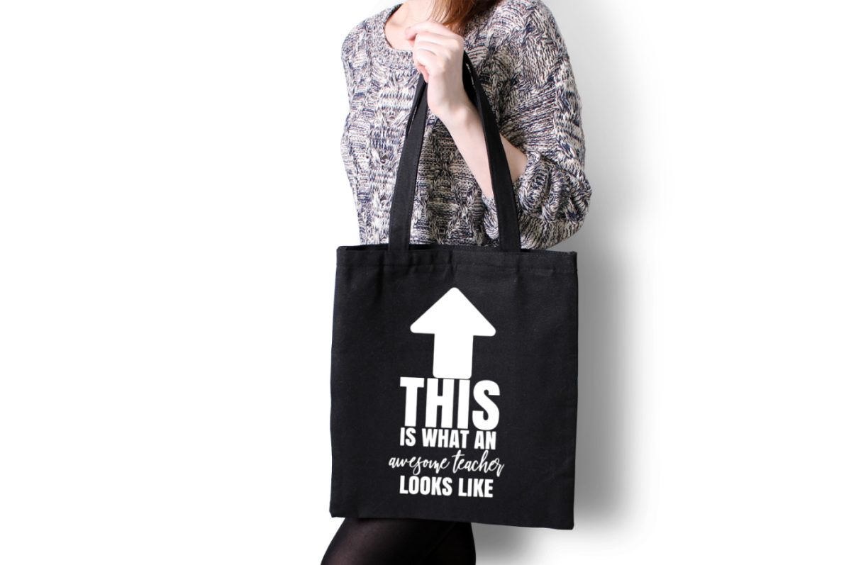 White woman holding a black tote bag with a design that says This is What an Awesome Teacher Looks Like