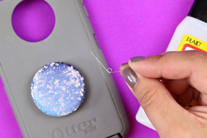 Woman's hand holding a safety pin near a phone case with a Pop Socket covered in Dimensional Magic
