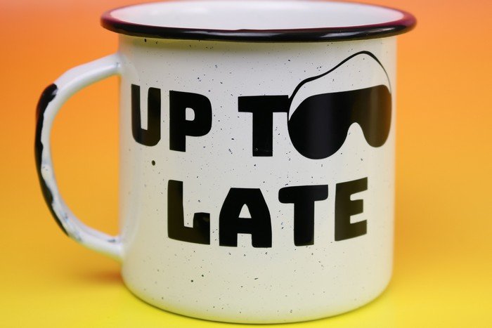A close up of a coffee mug with black Up Too Late vinyl