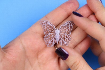 hands holding a small geometric butterfly embellishment made from liquid sculpey