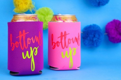 neon can koozies that say Bottoms Up in vinyl in front of a blue background