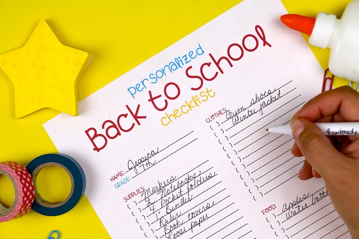 hand writing on a Back to School Checklist printable on a yellow background with school supplies