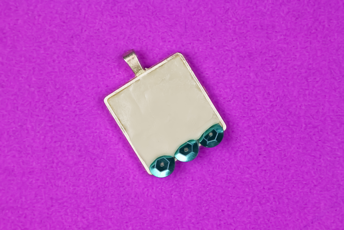 3 teal sequins embedded in jewelry clay in pendant bezel  on a purple background