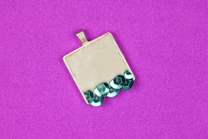 teal sequins embedded in jewelry clay in pendant bezel  on a purple background
