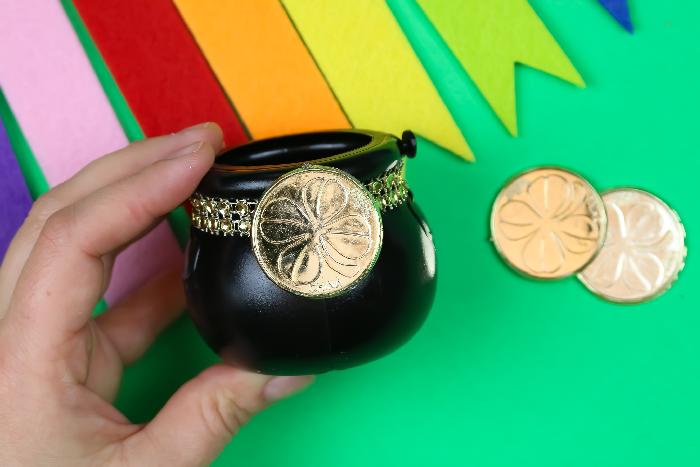 hand holding a mini pot of gold on a green background with rainbow bunting