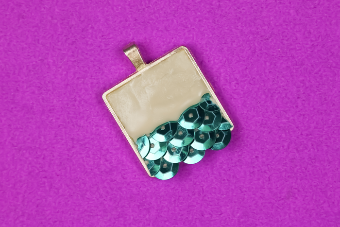 teal sequins embedded in jewelry clay in pendant bezel  on a purple background