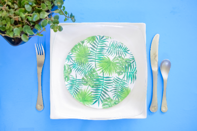Glass plates decoupaged with tropical paper on a white plate next to a plant