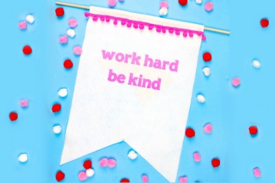 white felt banner that says work hard be kind on a blue background with pom poms