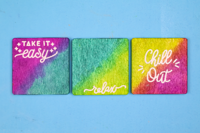 Colorful dyed wood coasters with white vinyl sayings on a blue background