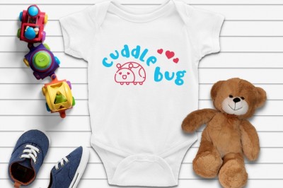 white baby onesie with a blue and pink cuddle bug SVG design next to toys