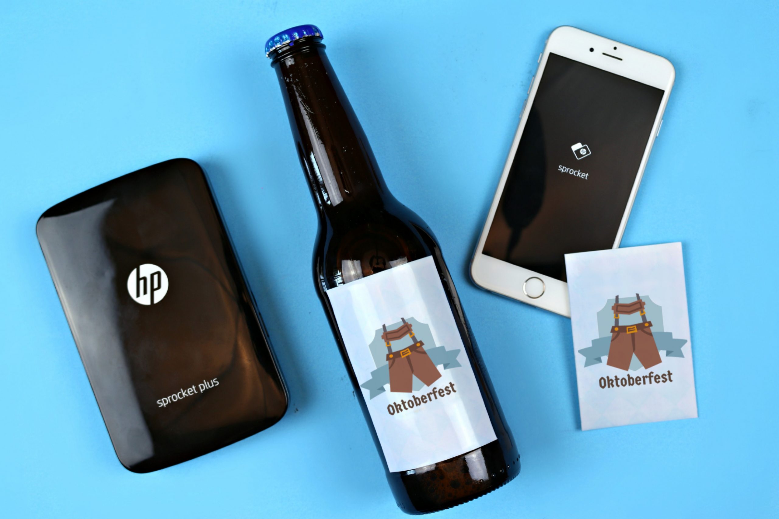 HP Sprocket, smartphone, Oktoberfest sticker and a beer bottle on a blue background