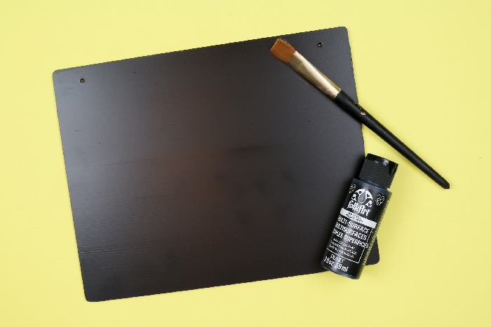 Black sign with paint and paintbrush on a yellow background