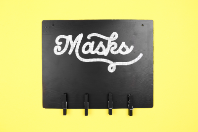Black mask sign with hooks on a yellow background