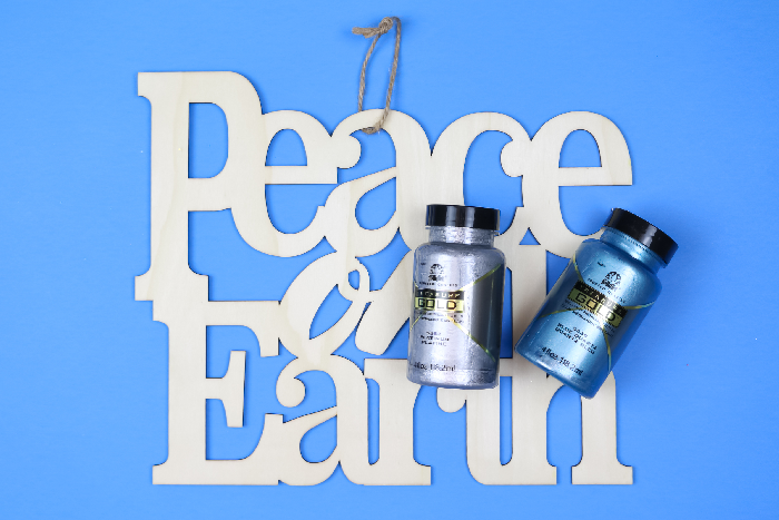 unpainted wood Peace on Earth sign with bottles of paint on a blue background