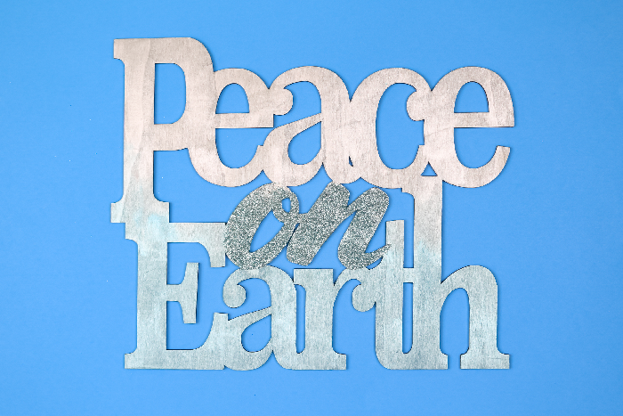 Painted and glittered Peace on Earth sign on a blue background