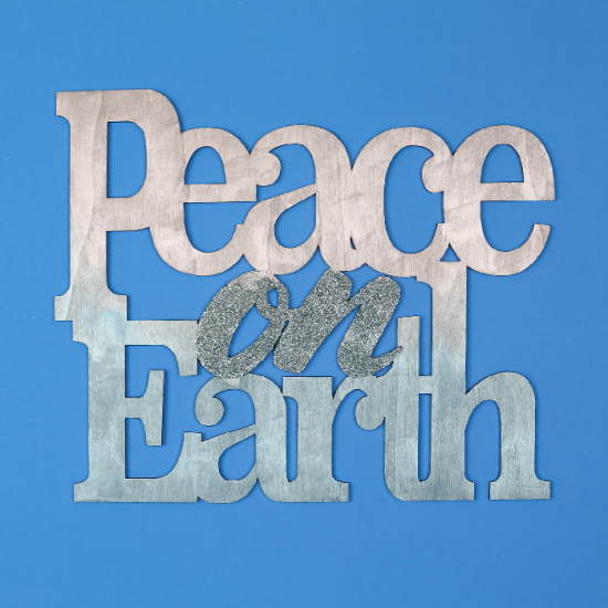 Painted and glittered Peace on Earth sign on a blue background
