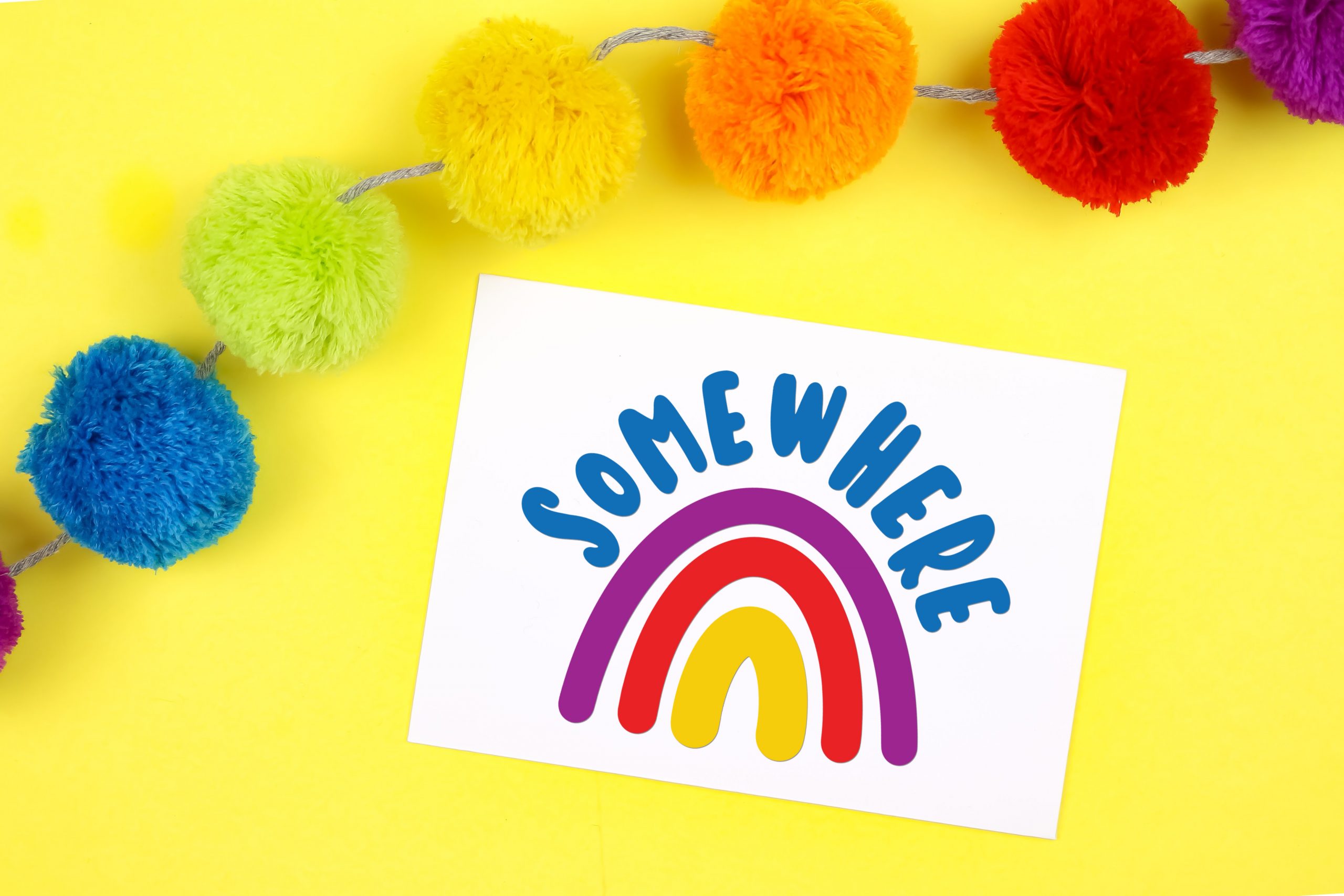 Colorful rainbow card on a yellow background with rainbow pom garland