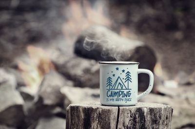 Camping is My Happy Place mug of hot steaming coffee sitting on an old log