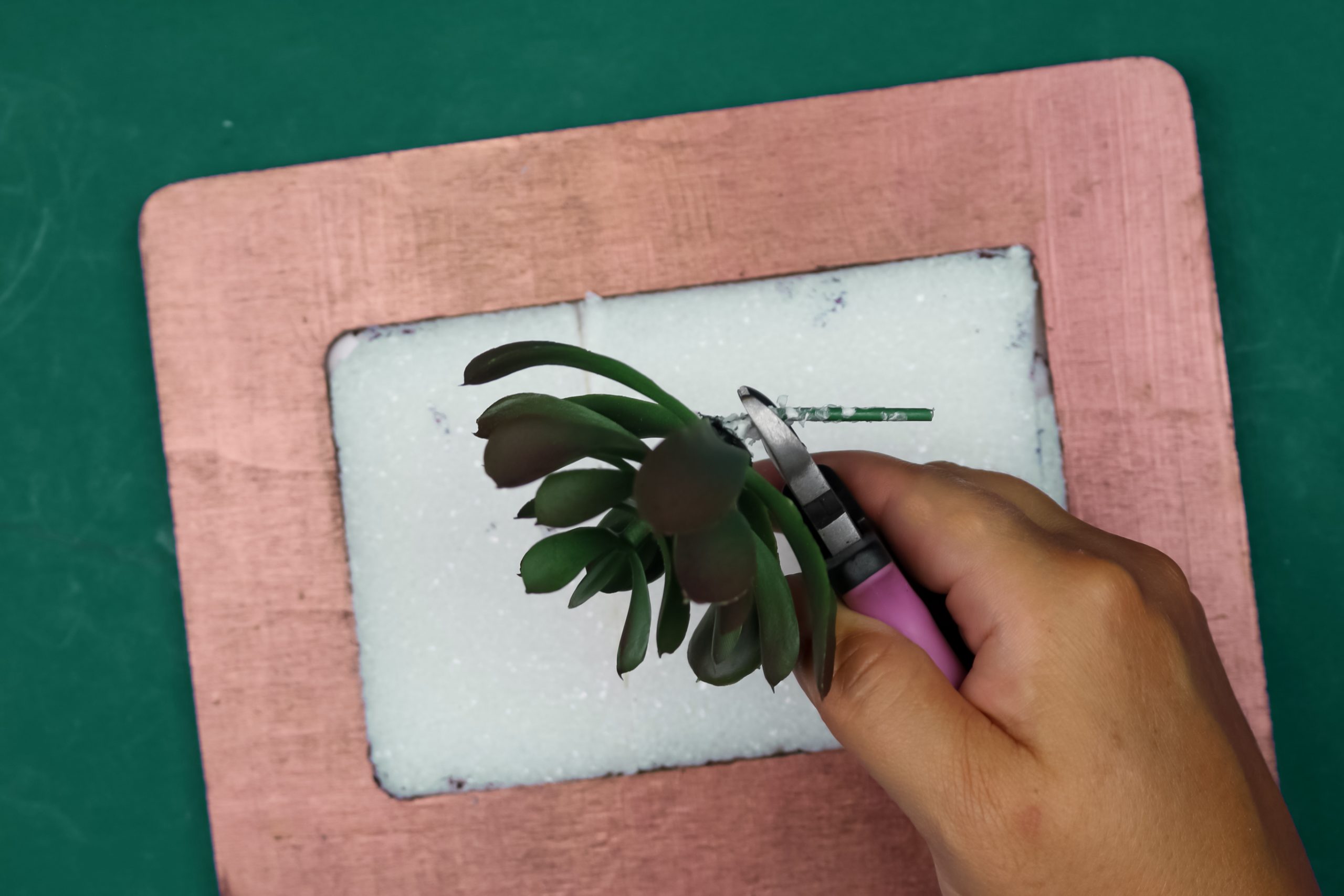 hand cutting the stem off of a faux succulent with wire cutters