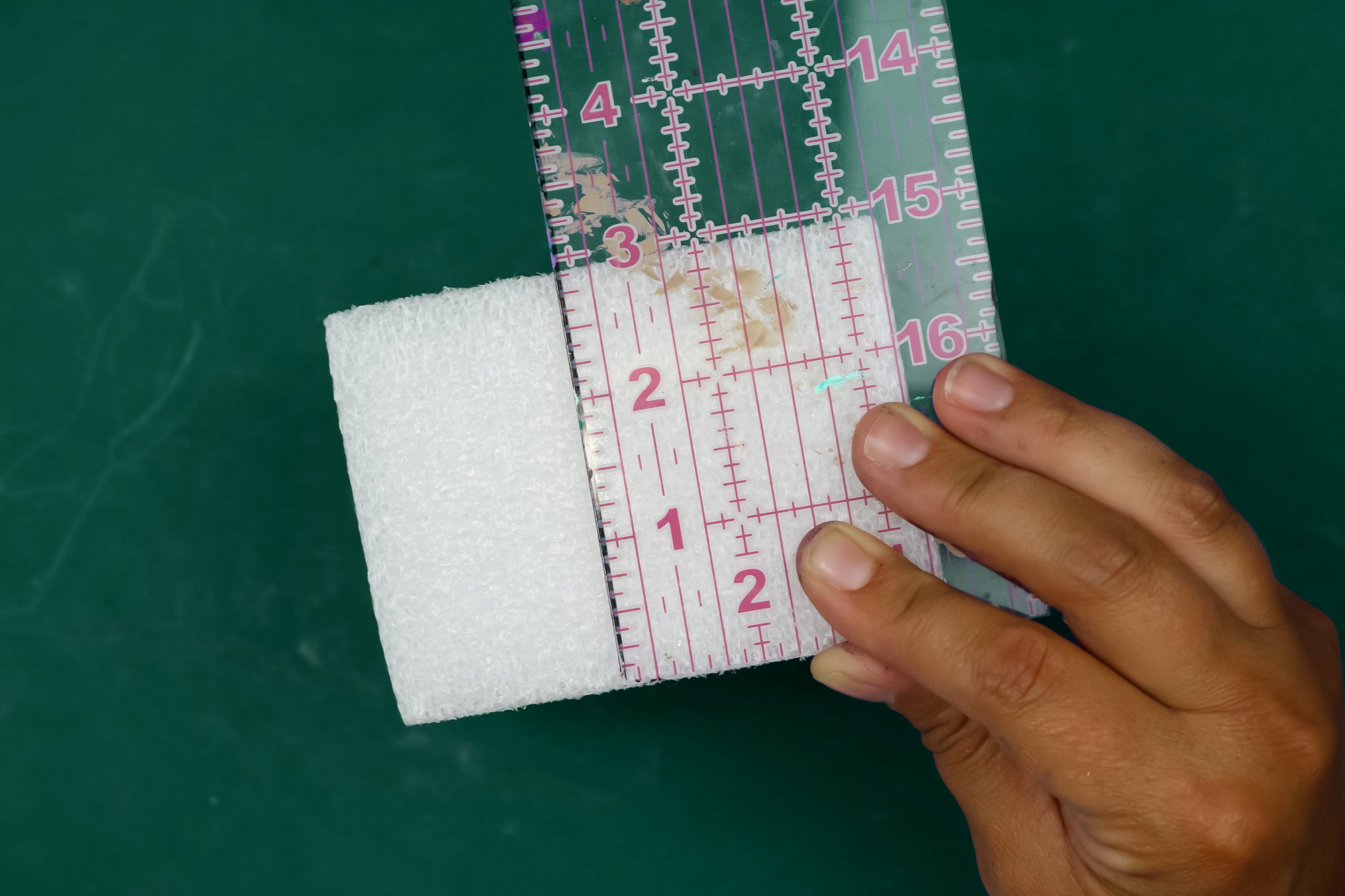 hand holding a ruler up to a block of white foam