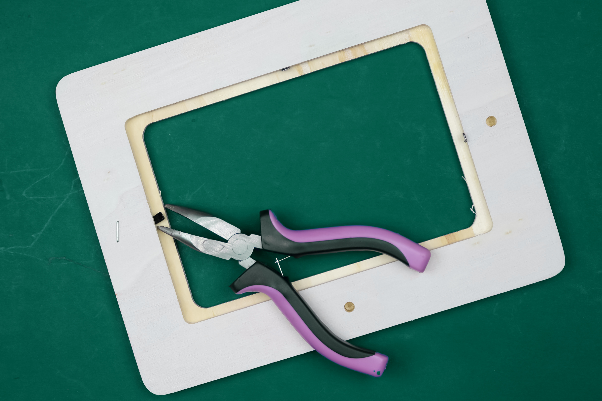 pliers pulling metal tab from a wood frame