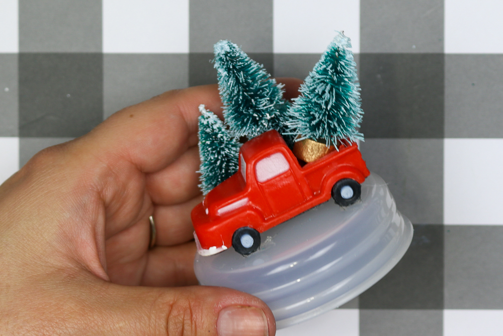 hand holding the base of a snow globe decorated with red truck and bottle brush trees