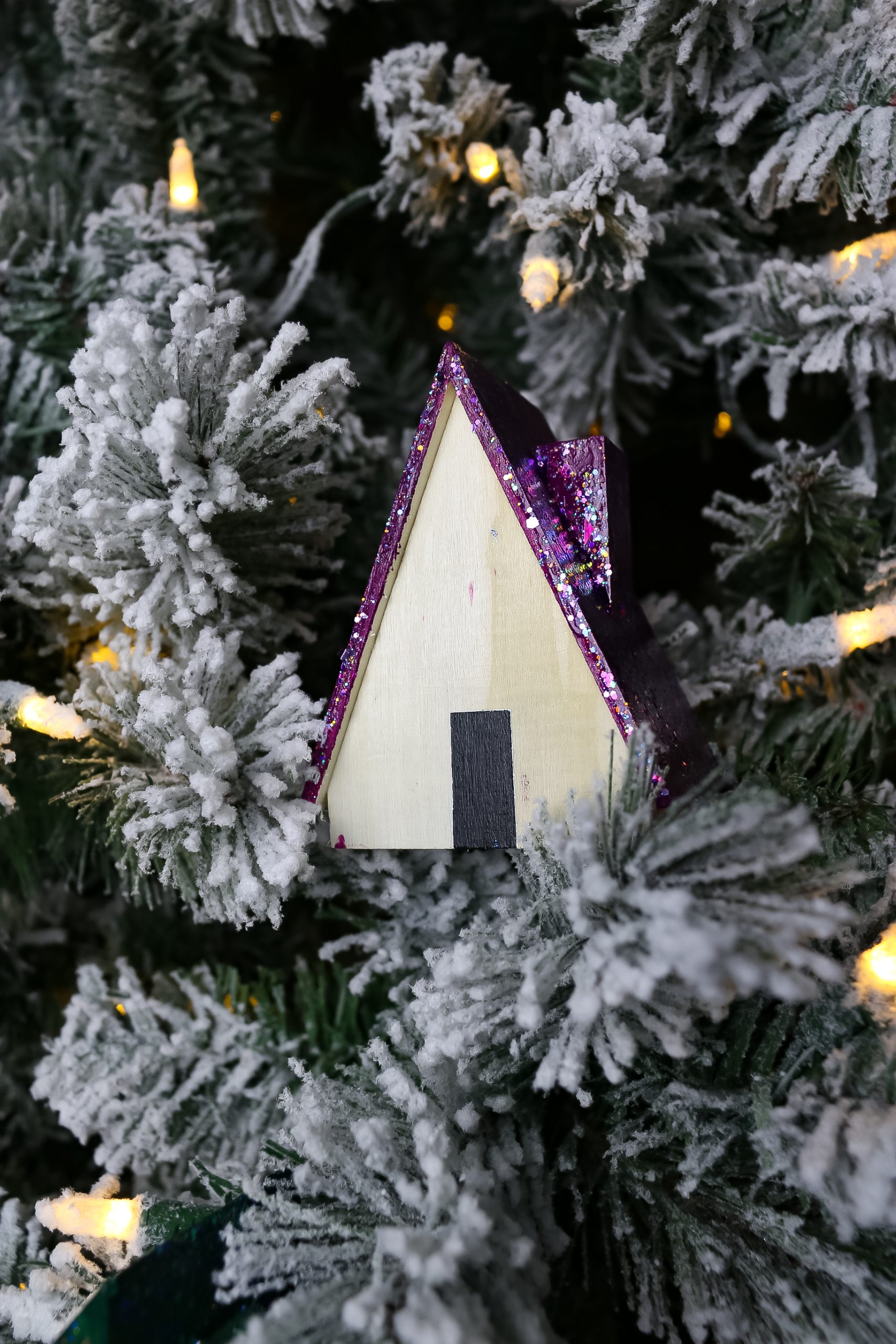 wood house with purple glittered roof in a flocked Christmas tree