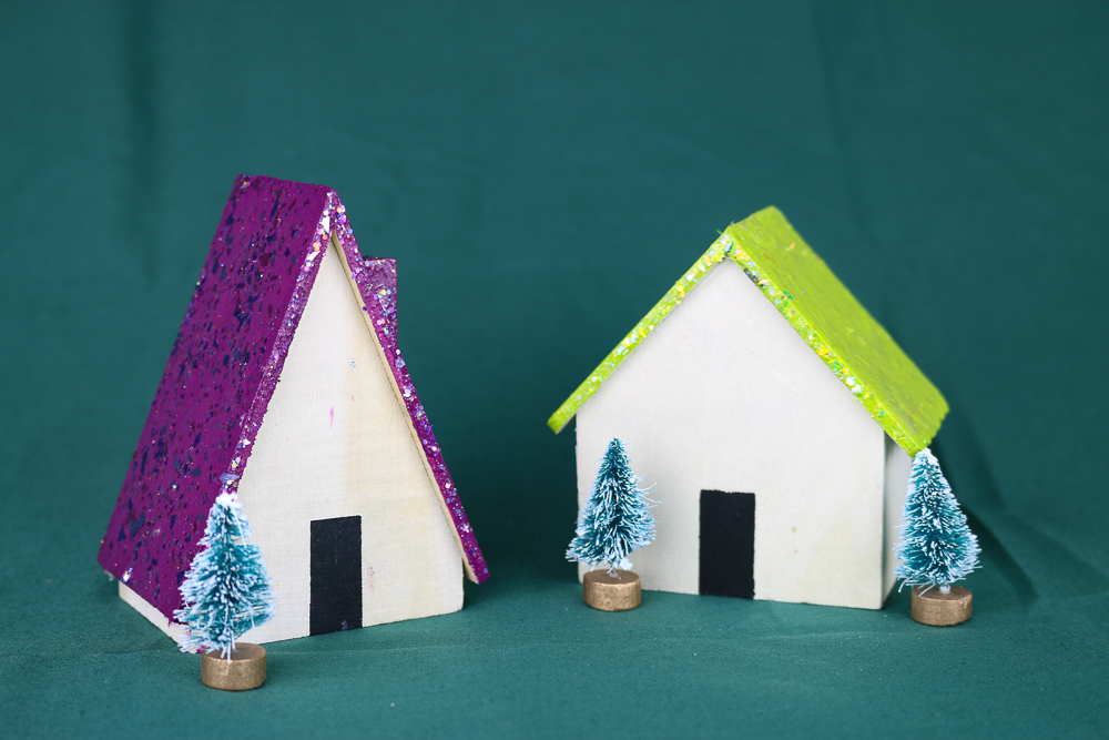two wood houses, one with purple glitter roof and one with a bright green glittered roof