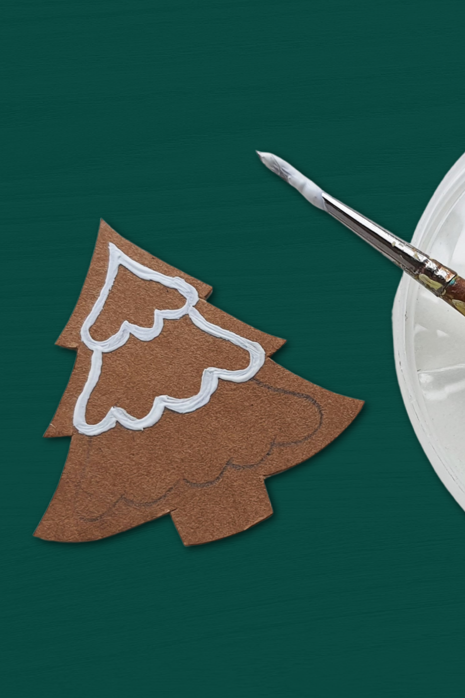 partially painted paper gingerbread tree ornament on a green background