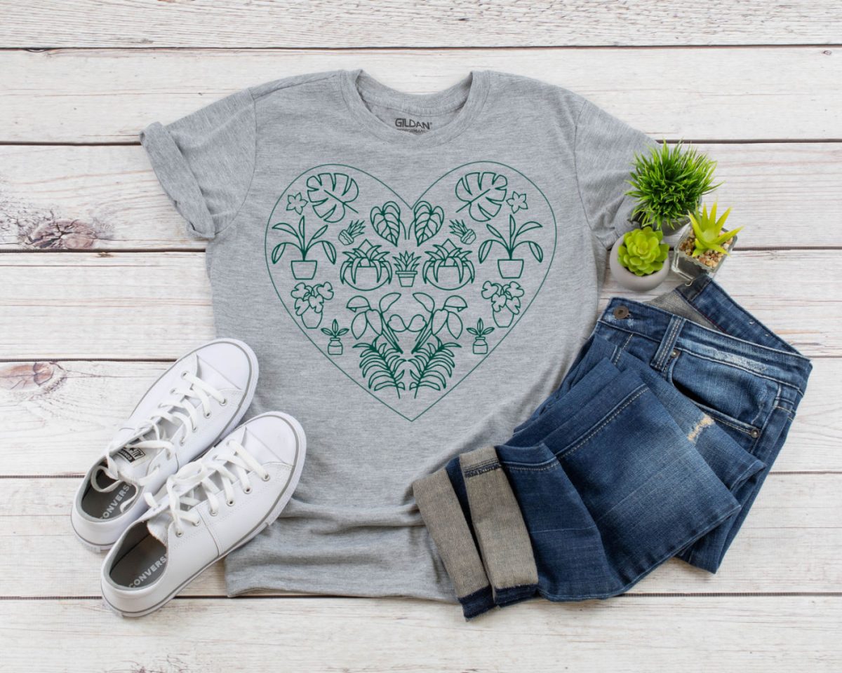Green plant heart SVG design on a grey shirt. The shirt is near shoes, jeans and a potted plant.