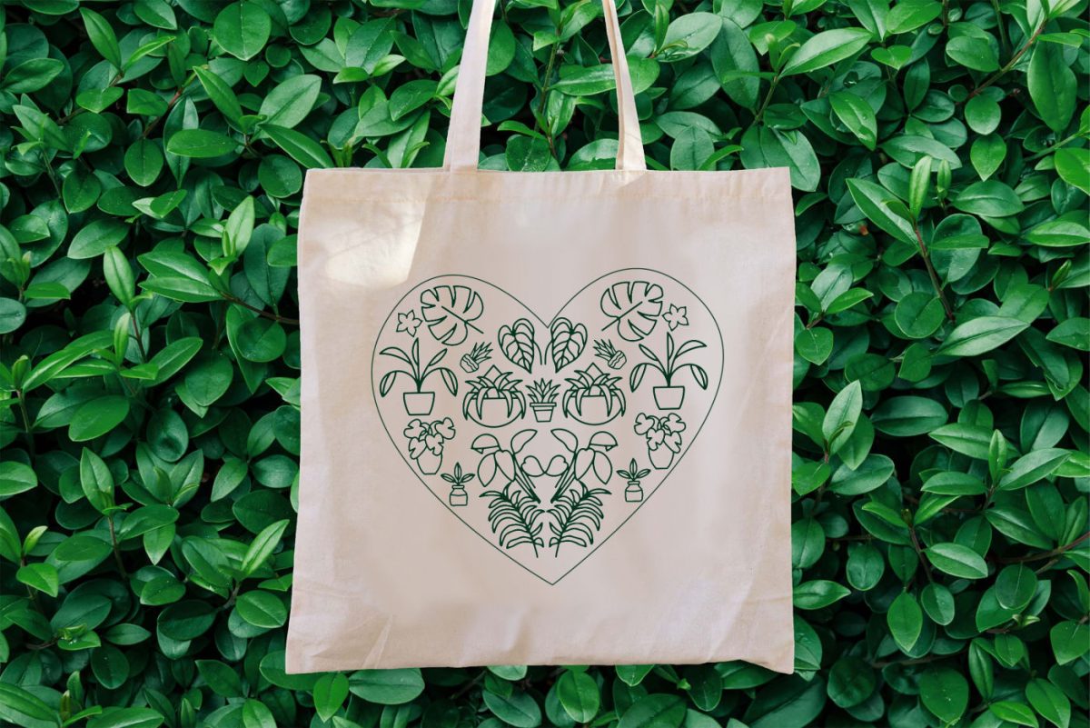 Green plant heart SVG in vinyl on a tote bag that is being held in front of a garden hedge.