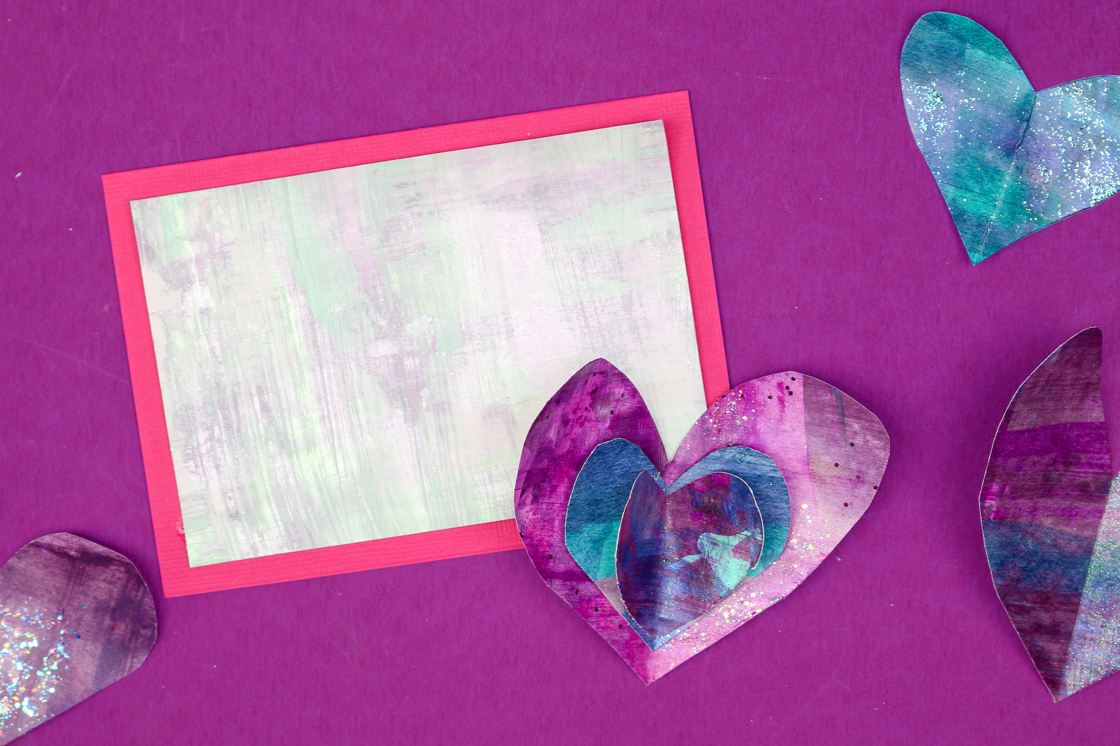pink cardstock topped with painted cardstock near stacked paper hearts