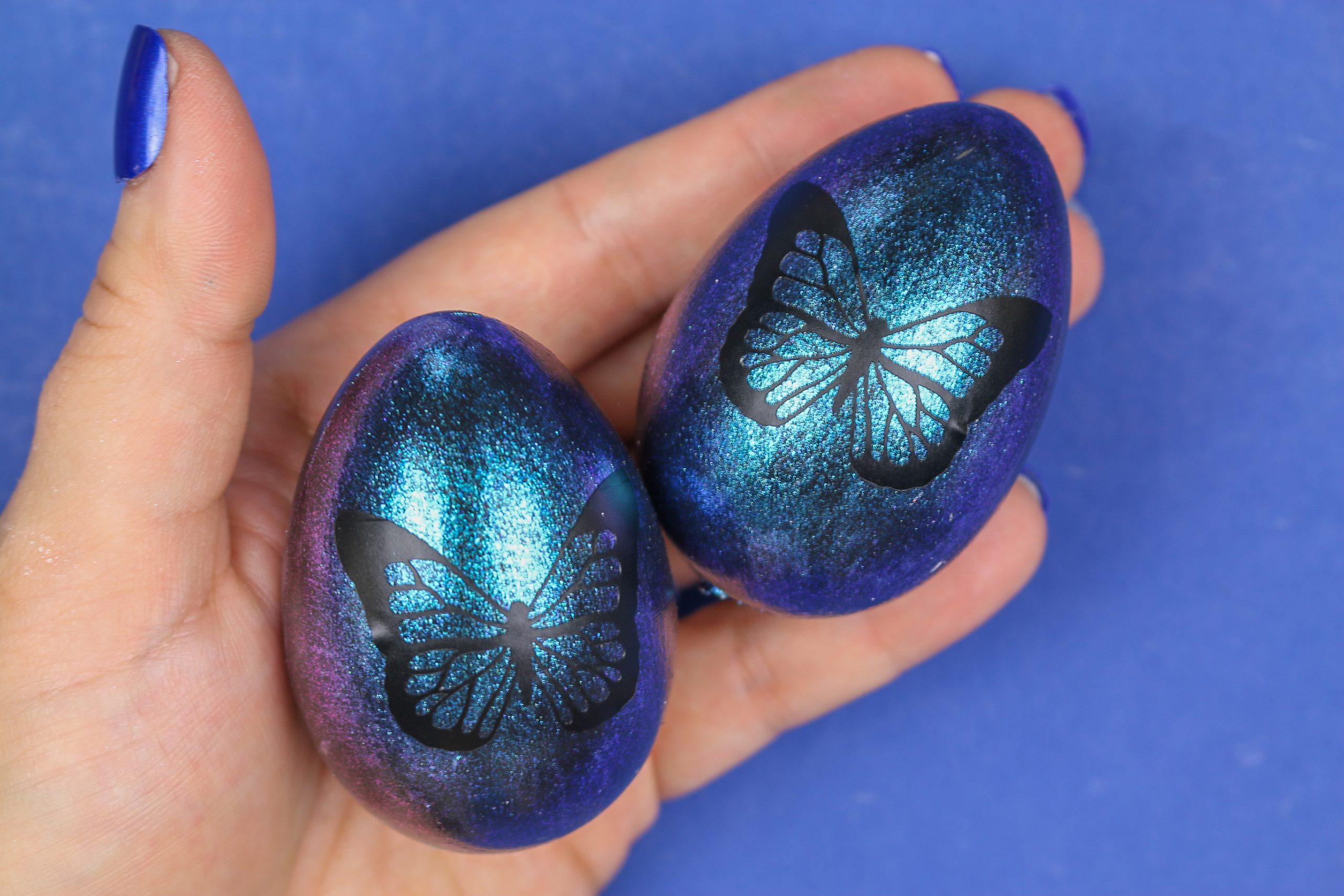 woman's hand holding two blue butterfly easter eggs