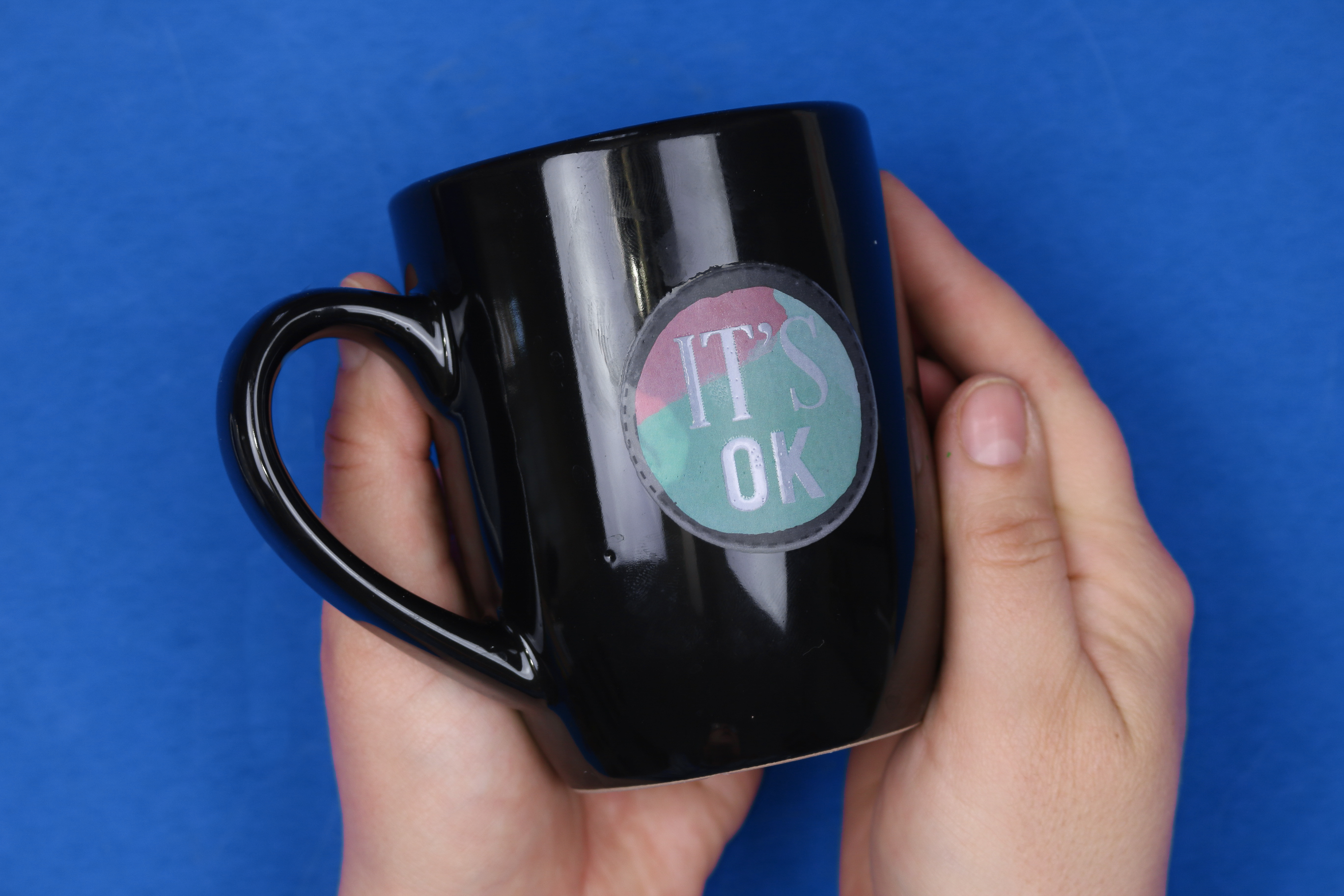 hand holding black mug with "It's OK" sticker