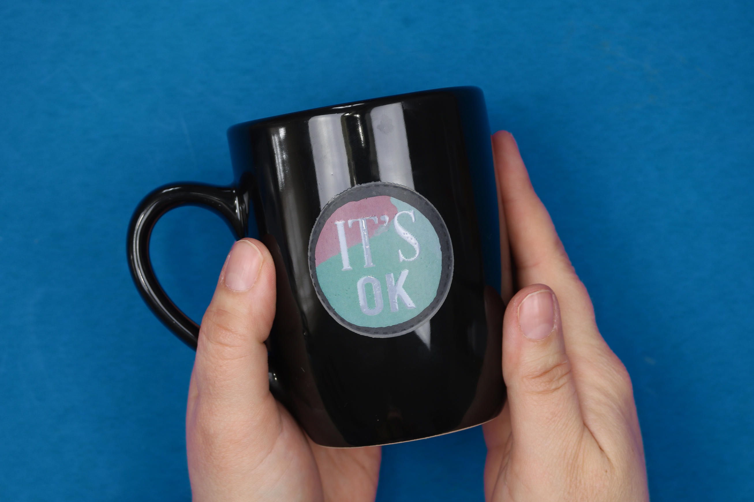 hands holding black mug with It's Ok sticker